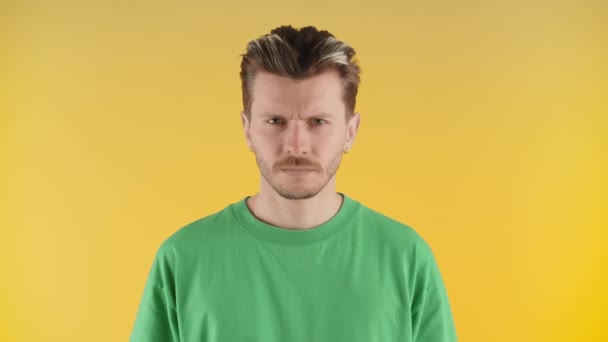 Egy borostás fiatalember áll a sárga falnál, és belenéz a kamerába. Egy rosszalló férfi zöld pólóban pózol a kamerának. Kiváló minőségű 4k felvételek - Felvétel, videó