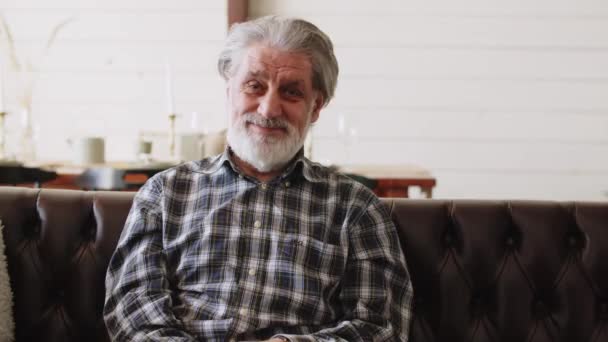 Sorridente bell'uomo anziano che guarda la macchina fotografica mentre è seduto sul divano a casa. Sentirsi felici. Filmati 4k di alta qualità - Filmati, video