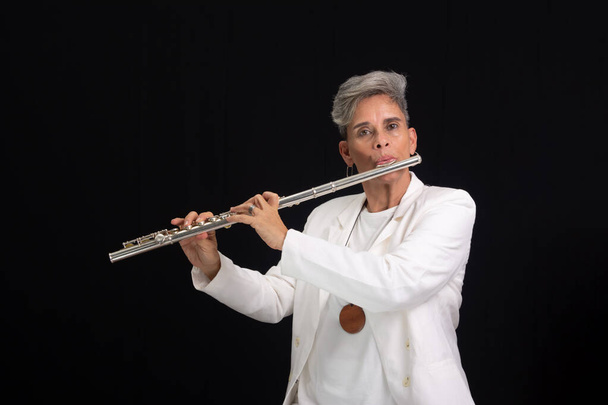 Hermosa mujer músico de pelo plateado con traje blanco tocando flauta transversal sobre fondo negro. - Foto, imagen