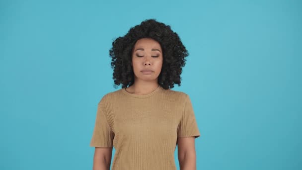 Frontale foto van een jonge zwarte vrouw met krullend haar. Afro-Amerikaanse vrouw poseert tegen een blauwe achtergrond tijdens een studio-shoot. Hoge kwaliteit 4k beeldmateriaal - Video