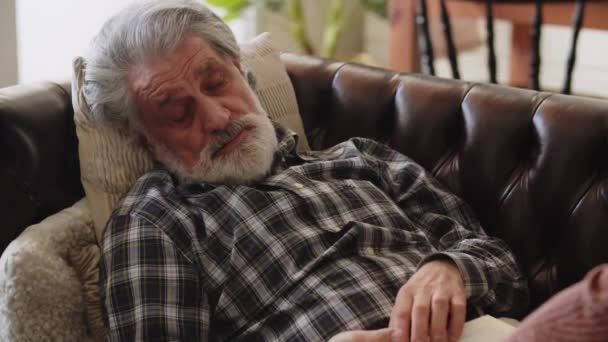 Un uomo dai capelli grigi si addormentò sul divano, tenendo in mano un libro. L'anziana moglie lo coprì con una coperta. Filmati 4k di alta qualità - Filmati, video