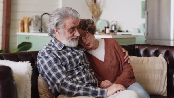 Fröhliches älteres grauhaariges verliebtes Paar, das sich entspannt auf dem Sofa im Wohnzimmer umarmt und lacht. Hochwertiges 4k Filmmaterial - Filmmaterial, Video