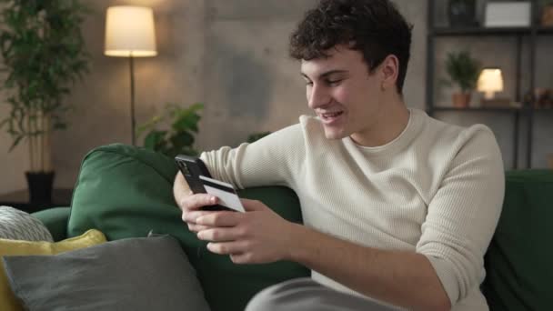 Yksi teini-ikäinen nuori mies valkoihoinen mies istuu kotona käyttää luottokorttia ostoksia verkossa käyttää internetiä online-ostoksia varten aktiivinen moderni verkkopankki - Materiaali, video