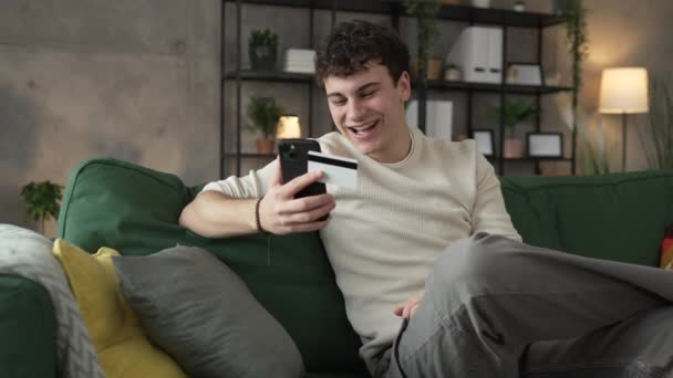 Yksi teini-ikäinen nuori mies valkoihoinen mies istuu kotona käyttää luottokorttia ostoksia verkossa käyttää internetiä online-ostoksia varten aktiivinen moderni verkkopankki - Materiaali, video