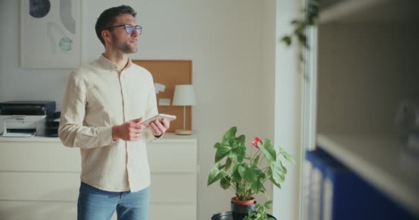 Serious male entrepreneur holding digital tablet while standing near plant at office - Footage, Video