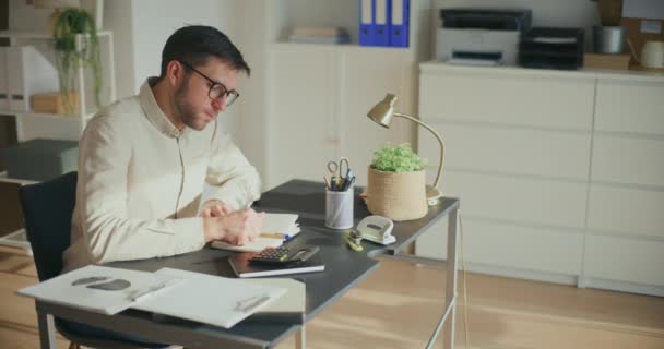 Уставший молодой предприниматель-мужчина берет перерыв, сидя за столом в офисе - Кадры, видео