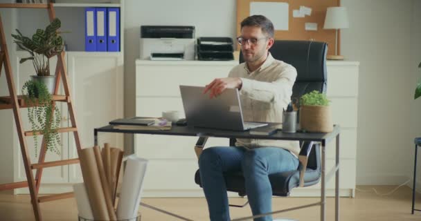Молодий чоловічий бізнес-професіонал починає роботу на ноутбуці, сидячи за столом в офісі - Кадри, відео