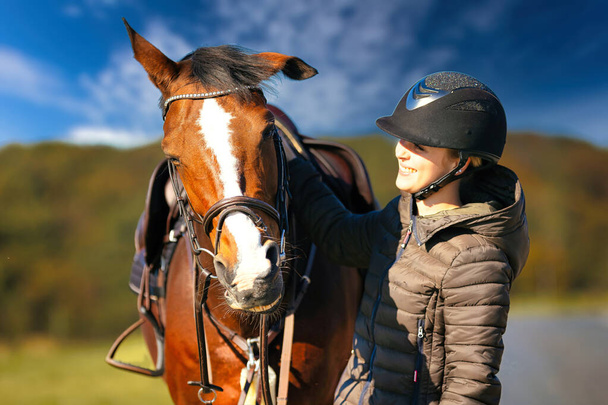 Portrait de la tête d'un cheval contre un ciel bleu, le cavalier se tient à côté du cheval. Une journée d'automne ensoleillée dans la nature. - Photo, image