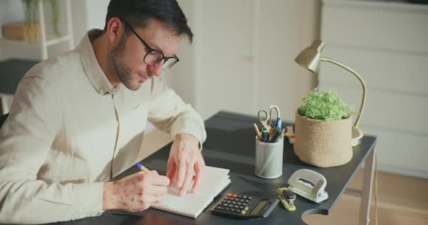 Frusztrált férfi vállalkozó elkészítése pénzügyi jelentés segítségével számológép, miközben ül az íróasztal az irodában - Felvétel, videó