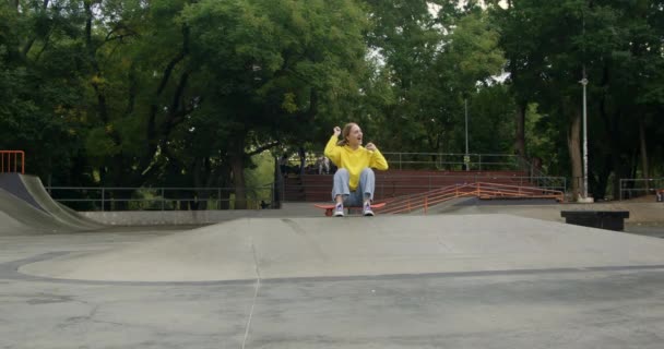 Mädchen auf Skateboard feuert blonde Freundin beim Tretroller-Fahren an. Teenager treiben im Skatepark am Frühlingswochenende Extremsport in Zeitlupe - Filmmaterial, Video