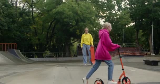 Deportivas adolescentes en skate park con monopatín y scooter. Los mejores amigos pasan las vacaciones al aire libre haciendo deporte extremo. Estilo de vida activo - Imágenes, Vídeo