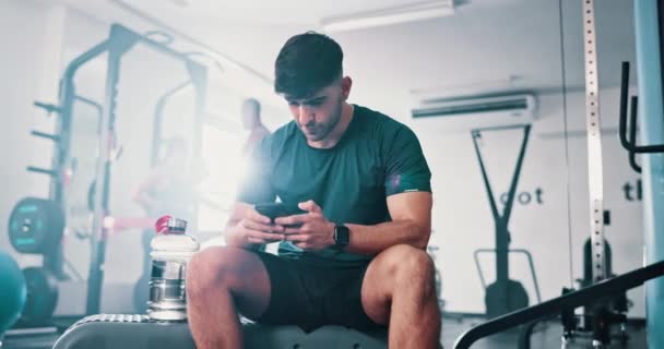Gym, phone or relax man reading online workout information, training instruction or fitness blog. Cellphone, mobile app and athlete check social media post on challenge, exercise or physical activity. - Footage, Video