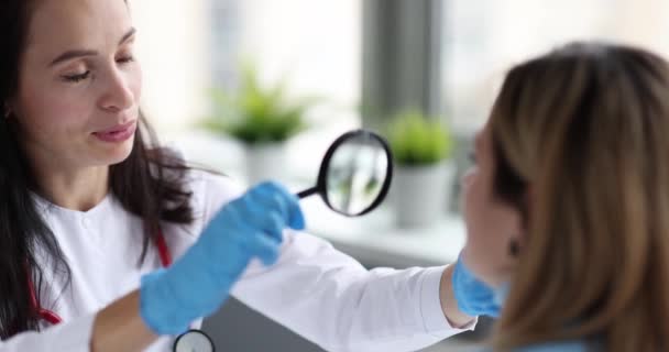 Lekarz kosmetolog badający skórę twarzy pacjenta szkłem powiększającym 4k film slow motion. Koncepcja leczenia trądziku - Materiał filmowy, wideo