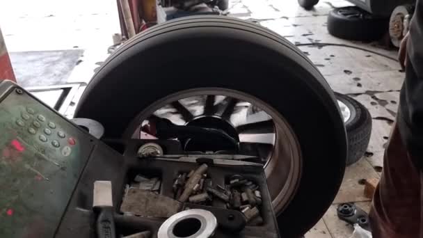 Primo piano del lavoratore che tenta di bilanciare il pneumatico dell'auto con la macchina di bilanciamento della ruota in officina garage - Filmati, video