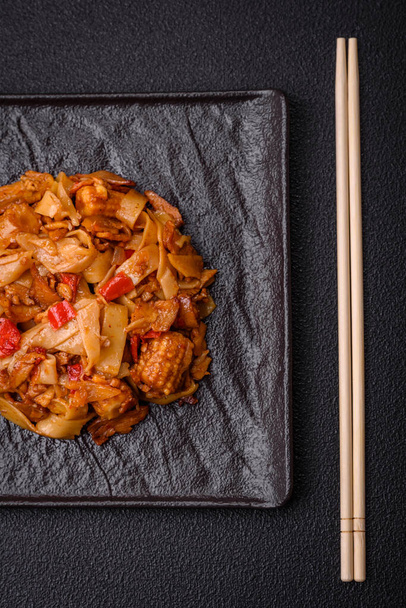Heerlijke Aziatische udon schotel met groenten, champignons, zout en specerijen op een keramische plaat op een donkere betonnen achtergrond - Foto, afbeelding