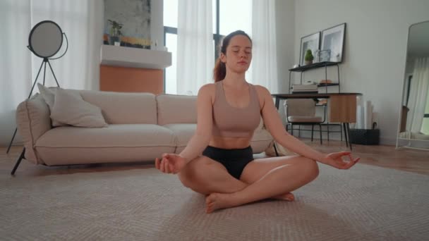 молода жінка одягнена в активний одяг, що практикує йогу вдома фітнес і оздоровлення в квартирі - Кадри, відео