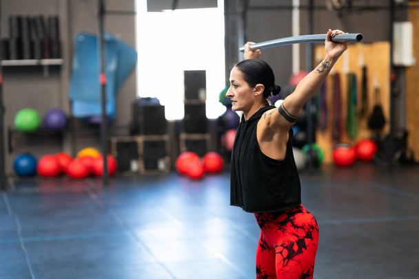 Horizontal photo with copy space of a mature woman warming up and stretching with a bar in a cross training gym - Photo, Image