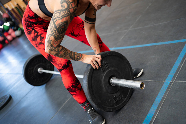 Close-up of an unrecognizable fit woman adding weight plates to a bar for weightlifting - Photo, Image