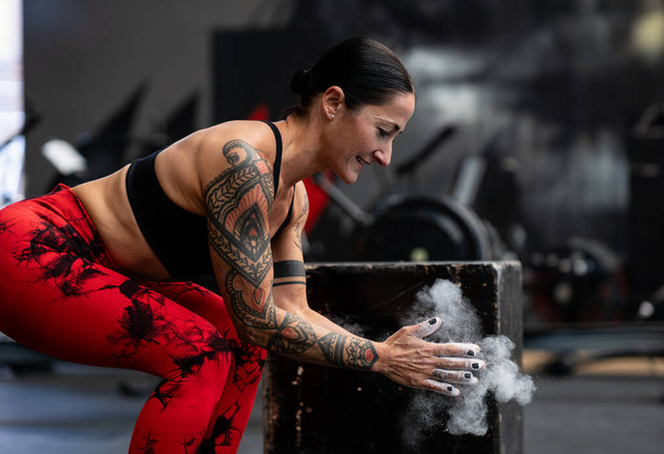 Magnesium dust floating from the hands of a sporty woman about to lift weights - Photo, Image