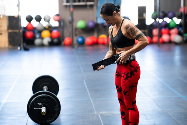 Strong woman preparing to weightlifting using safety belt in a cross training gym - Photo, Image