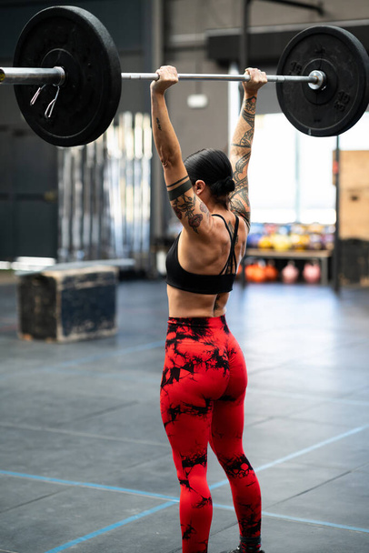 Vertical rear view of a mature sportive and strong woman bodybuilding in a gym - Photo, Image