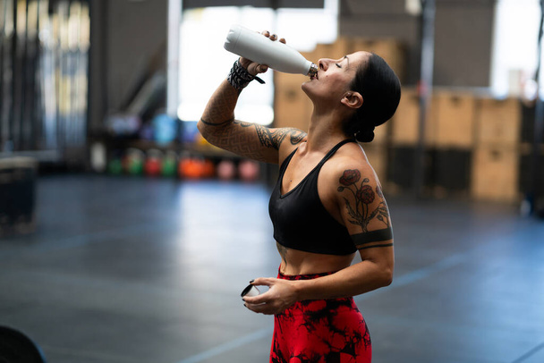 Side view of a fit woman drinking water form a reusable bottle in a gym - Photo, Image