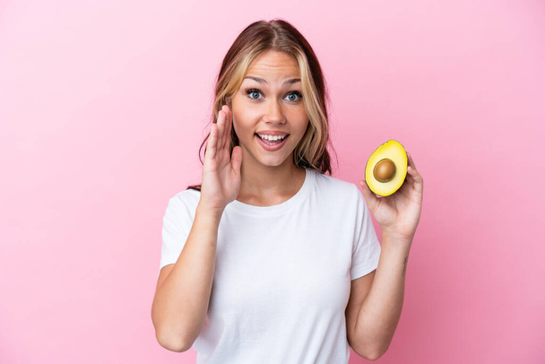 Young Russian woman holding avocado isolated on pink background with surprise and shocked facial expression - Photo, Image