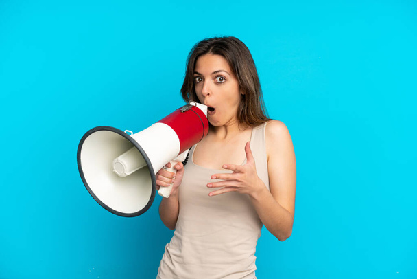 Young caucasian woman isolated on blue background shouting through a megaphone with surprised expression - Photo, image