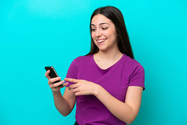 Jong meisje geïsoleerd op blauwe achtergrond verzenden van een bericht of e-mail met de mobiele - Foto, afbeelding