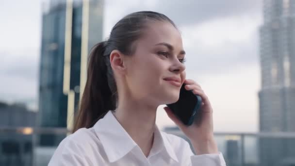 笑顔のビジネス女性は,午後の都市と高層ビルの背景に彼女の携帯電話で話し,現代の都市フリーランサーのライフスタイル. 高品質の4k映像 - 映像、動画