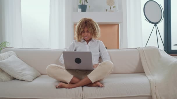 mujer navegando por Internet con el ordenador portátil sentado en el sofá en la sala de estar mirando cámara amable sonriendo - Imágenes, Vídeo