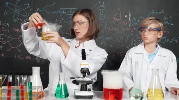 Smart caucasian teacher mixing chemical liquid in science laboratory. Professional instructor doing experiment in STEM science class with microscope at blackboard written chemical theory. Erudition. - Footage, Video