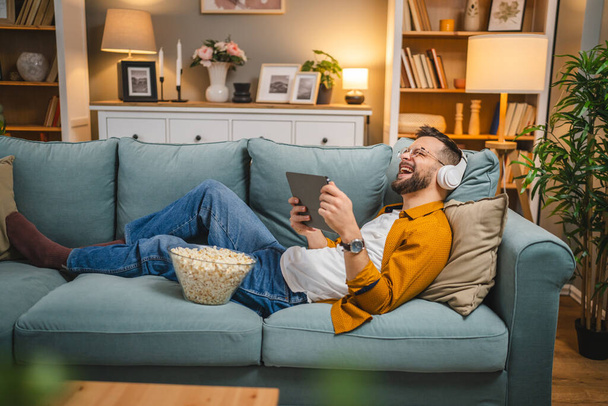 Un uomo adulto caucasico maschio sul divano letto a casa guardare film video online utilizzare tablet digitale o avere una videochiamata - Foto, immagini