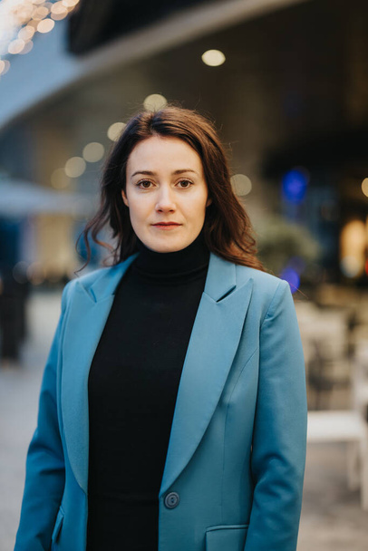 A portrait of a woman with a serious expression, wearing a blue blazer and black turtleneck, on an urban background. - Photo, Image