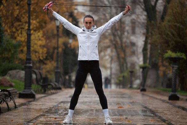 Young woman training in rainy park. Female jogger exercising outdoors  - Photo, Image