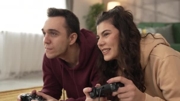 大人のカップル男性と女性の慎重な夫と妻またはボーイフレンドとガールフレンドは,自宅でコンソールビデオゲームをプレイするジョイスティックコントローラーは楽しいレジャーの喜びと絆の概念を持っています - 映像、動画