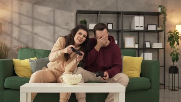 Dospělí pár muž a žena kavkazský manžel a manželka nebo přítel a přítelkyně hrát konzole videohry doma držet joystick regulátor bavit volný čas radost a bonding koncept - Záběry, video
