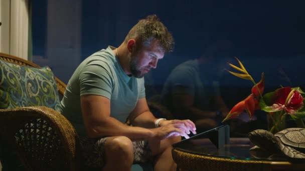 Homme mûr tapant sur l'écran de la tablette email ou contenu de blog de médias sociaux à la fin de la nuit. Focalisé gars regardant l'écran lumineux de l'appareil technique. Homme d'affaires travaillant en ligne à distance sur les vacances tropicales - Séquence, vidéo