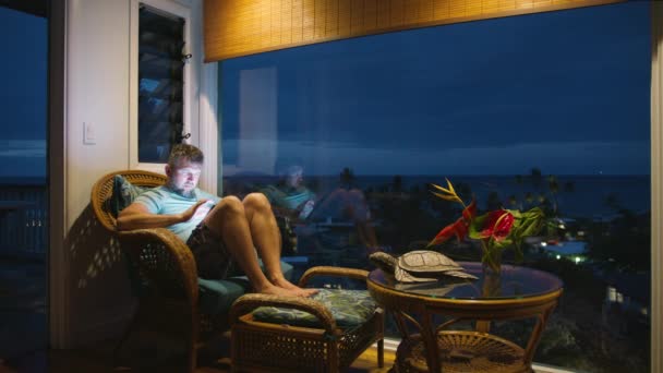 Focalisé gars regardant l'écran lumineux de l'appareil technique. Homme d'affaires travaillant en ligne à distance sur les vacances tropicales. Dactylographie masculine détendue sur l'écran de la tablette email ou contenu de blog de médias sociaux à la fin de la nuit - Séquence, vidéo