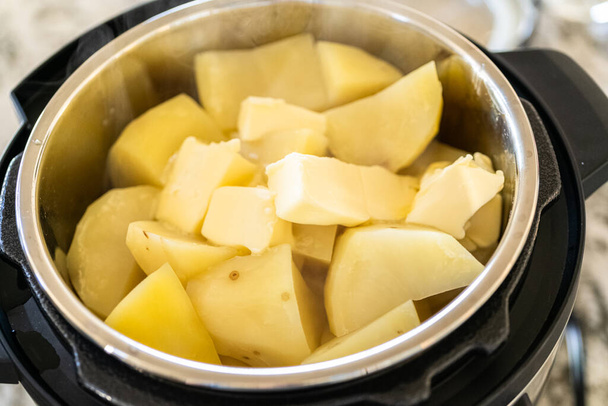 Σε μια κομψή μοντέρνα κουζίνα, ετοιμάζοντας βελούδινο πουρέ πατάτας χρησιμοποιώντας μια χύτρα πίεσης για ένα γρήγορο και νόστιμο γεύμα. - Φωτογραφία, εικόνα