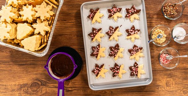 Preparando galletas en forma de estrella, medio sumergidas en chocolate, acentuadas con chispas de chocolate con menta para las fiestas. - Foto, Imagen
