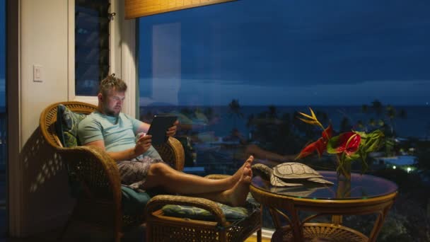 Homme d'affaires travaillant en ligne à distance sur l'île tropicale vacances. Dactylographie masculine détendue sur l'écran de la tablette e-mail ou blog de médias sociaux tard dans la nuit. Focalisé gars regardant l'écran lumineux de l'appareil technique - Séquence, vidéo