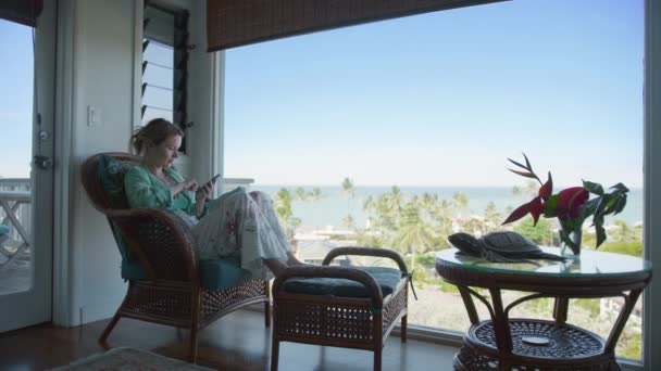 Зосереджена дама дивиться на екран мобільного телефону. Ділова жінка працює дистанційно на тропічних канікулах. Розслаблена жіноча прокрутка на екрані смартфона, читання електронних листів або блог соціальних мереж з видом на океан - Кадри, відео