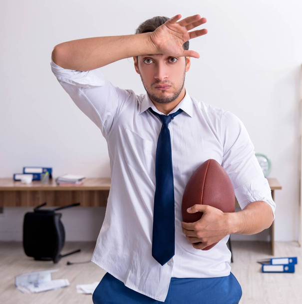 Junger Mitarbeiter wirft Rugbyball im Büro - Foto, Bild