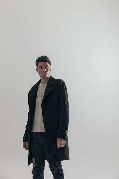 gros plan de jeune homme en manteau noir regardant de côté sur fond gris - Photo, image
