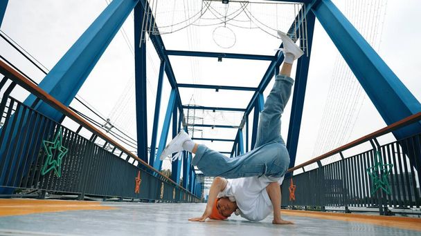 Dançarino break profissional executar passo de dança de rua na ponte. Asiático hipster usar fone de ouvido enquanto faz pose de congelamento. Dançarina, dançarina de rua conceito freestyle. Desporto ao ar livre 2024. Sprightly. - Foto, Imagem