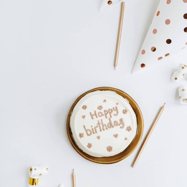 Elegante torta di compleanno con segno "Buon compleanno", candele, coni festivi su sfondo bianco. Concetto estetico di celebrazione di eventi festivi. Posa piatta, vista dall'alto. Colori bianco e oro - Foto, immagini