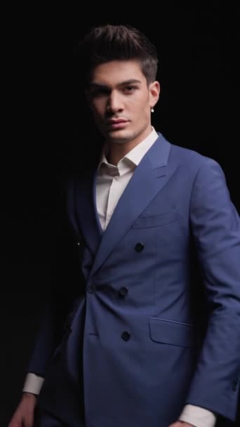 mysterious young businessman in blue suit walking, being confident, rubbing palms and looking to side in front of dark background - Footage, Video