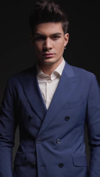 sexy elegant man in blue suit looking to side, holding hands in pockets and confidently posing in front of dark background with thunder lights - Footage, Video