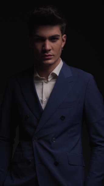 Nahaufnahme eines attraktiven männlichen Modells im blauen Anzug, das sich auf dunklem Hintergrund bewegt und dreht, während es Taschen hält - Filmmaterial, Video